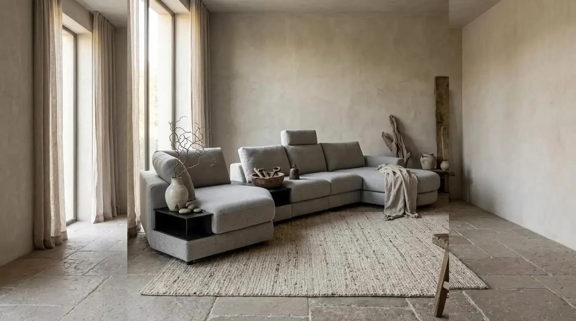 Grijze hoekbank Mirable met chaise longue en zwarte tussentafel voor een gepleisterde wand op een jute vloerkleed