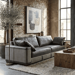 Zwarte leren bank in industrieel interieur met brick wall en grote raampartijen, ontworpen door Mokana Meubelen.