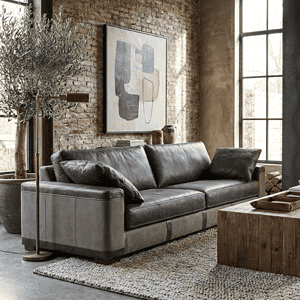 Zwarte leren bank in industrieel interieur met brick wall en grote raampartijen, ontworpen door Mokana Meubelen.