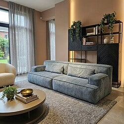 Zwarte houten boekenkast met planten en decoratie in een modern woonkamer met een comfortabele bank, perfect voor stijlvolle wooninrichting en meubeldesign van Mokana Meubelen.