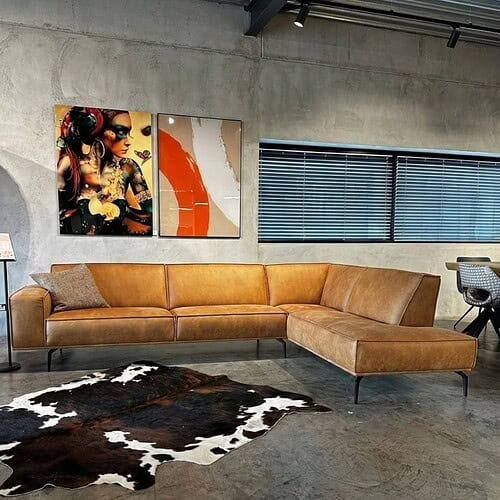Modernes Ecksofa aus Leder in Karamellfarbe, schlichtes Design für stilvolle Wohnzimmer, kombiniert mit farbenfrohen Kunstwerken und einem Tierfellteppich, perfekt für trendige Interieurs.