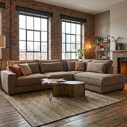 Ubeige stoffen hoekbank in loft stijl met grote ramen en industriële bakstenen muur, gecombineerd met houten details en groene planten voor een warme en stijlvolle woonkamer.