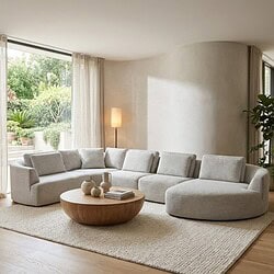 Lichtgrijze moderne L-vormige woonkamerbank met bijpassende vloerkleed, natuurlijke houten salontafel en grote ramen met uitzicht op de tuin, passend bij Mokana Meubelen.