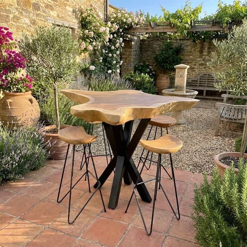 Houten barkrukken en een biertafel in een sfeervolle tuin met bloemen en terras, ambachtelijke meubels in natuurlijke materialen, perfecte tuinmeubelen voor buitengebruik, stijlvol en duurzaam design van Mokana Meubelen.