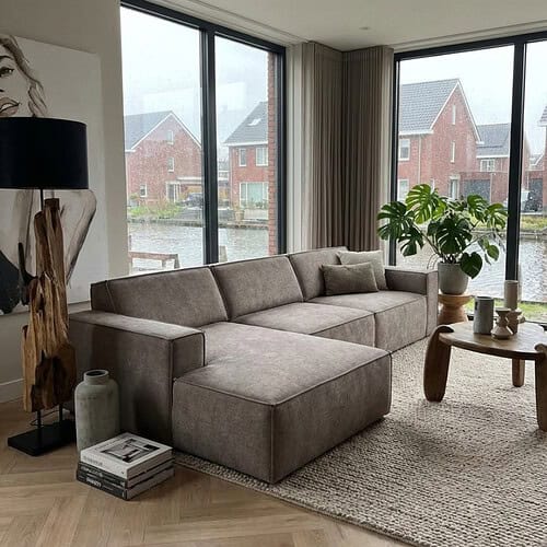 1. Luxe hoekbank van Mokana Meubelen in een modern wooninterieur met grote raampartijen en uitzicht op een waterkanaal, perfect voor stijlvolle en comfortabele zithoek.