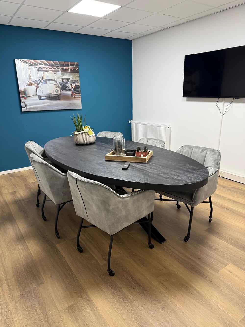 Modern eettafel met donker houten blad en metalen poten, omringd door stijlvolle comfortabele stoelen in een eigentijds interieur met een opvallende blauwe accentmuur.