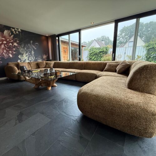 Ein langes, modernes Sofa mit weichen Kissen in einem stilvollen Wohnzimmer mit großen Fenstern und Gartenblick unterstreicht Luxus und Komfort.