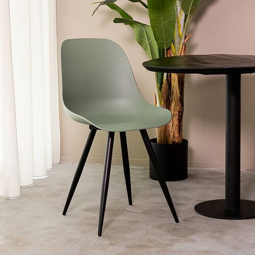 Modern design eetkamerstoel met lage zwart houten poten en mintgroene kuip. Perfect voor een stijlvol interieur, gecombineerd met een zwart rond eettafel en een groene plant voor een natuurlijke sfeer.