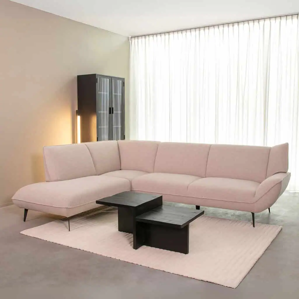 Lichtroze moderne hoekbank met slanke zwarte poten op een lichte vloerkleed in een minimalistische woonkamer.