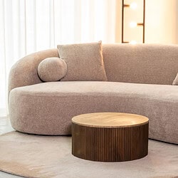 Sfeervol beige stoffen bank met ronde armleuningen en sierkussens, gecombineerd met een ronde houten salontafel in een modern interieur. Perfect voor een stijlvolle en gezellige woonkamer.