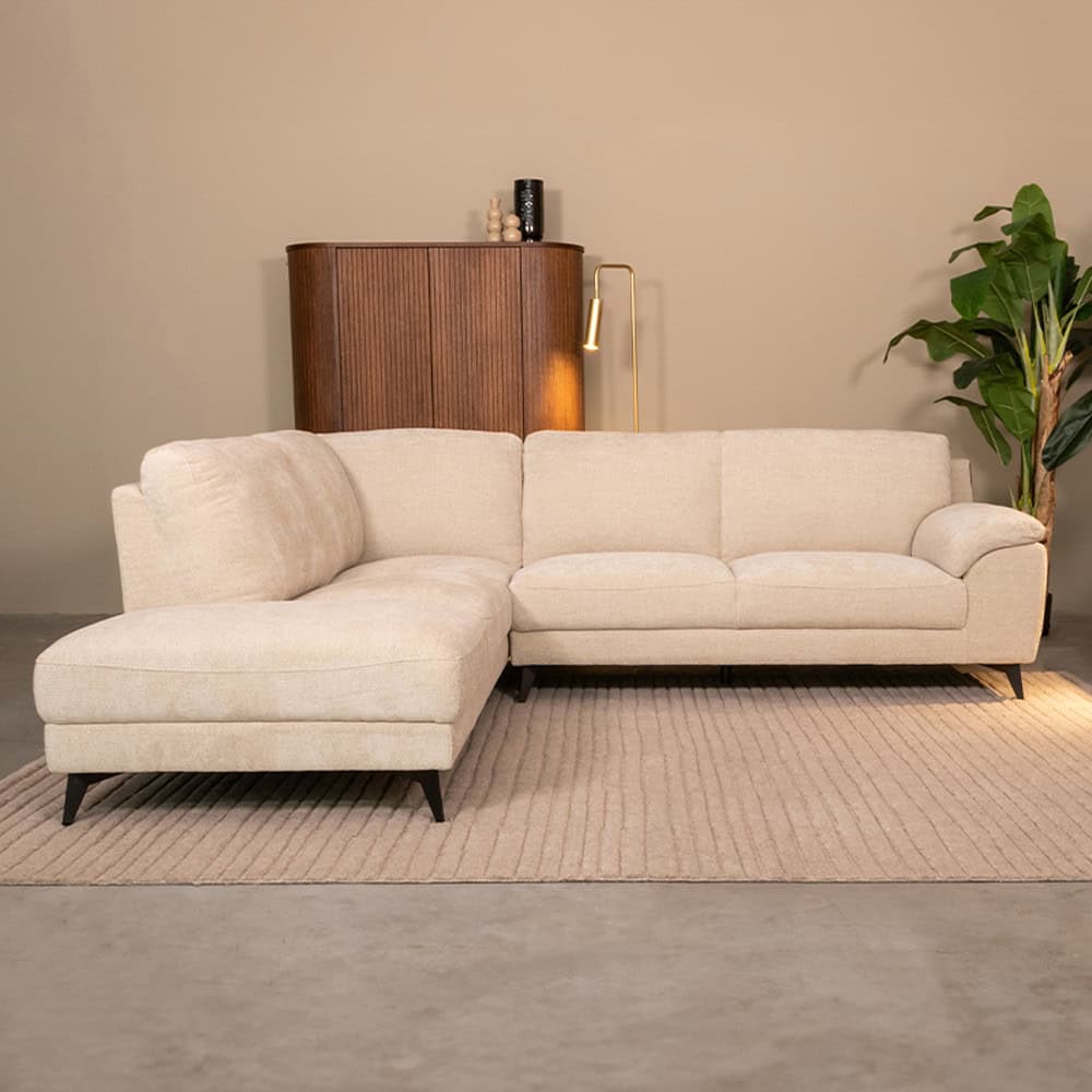 Comfy beige L-vorm bank met kussens en slanke zwarte poten in een modern interieur.