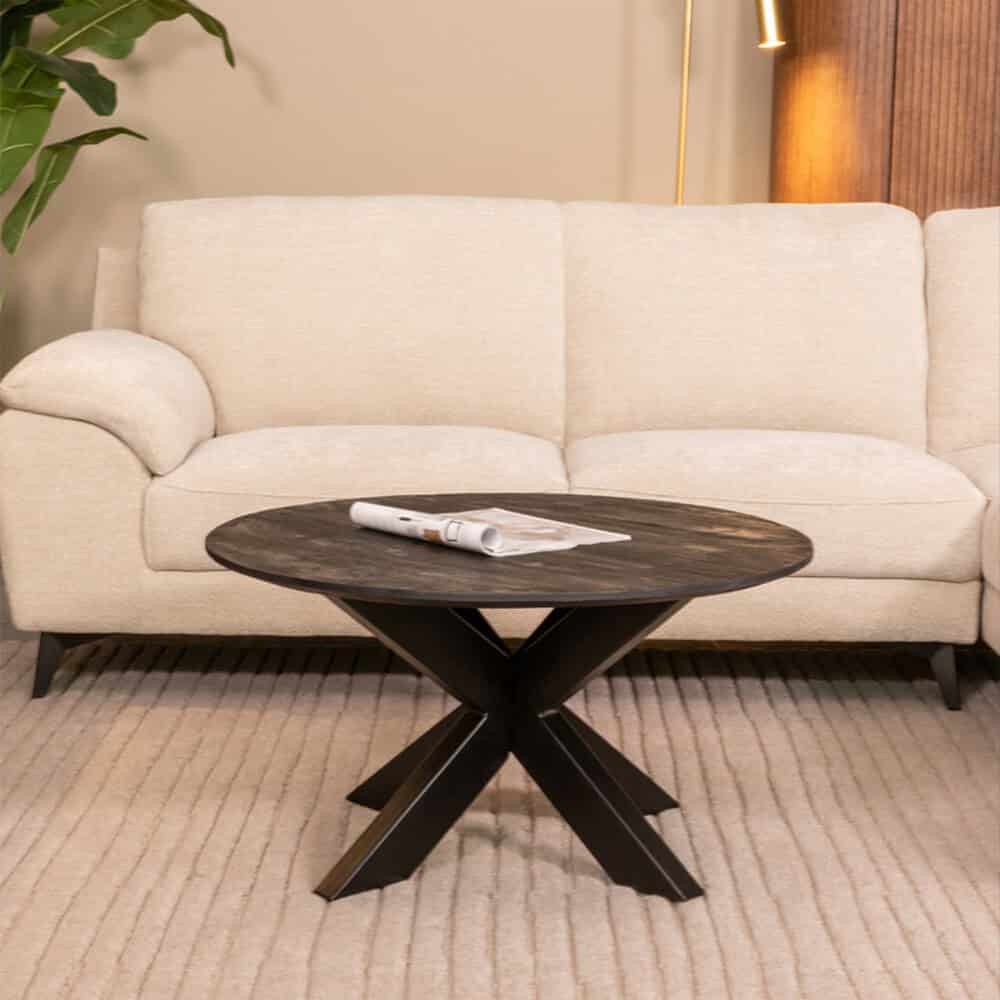 Lichte stoffen bank met houten poten in een modern interieur, gecombineerd met een zwart houten salontafel en een plant op de achtergrond.