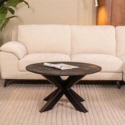 Lichte stoffen bank met houten poten in een modern interieur, gecombineerd met een zwart houten salontafel en een plant op de achtergrond.