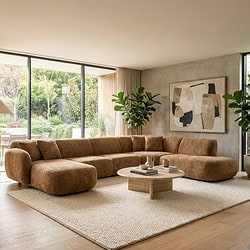 Lage resolutie, moderne hoekbank in warm bruin textile met bijpassende salontafel in hout, in een sfeervol huis met grote raampartijen en groen uitzicht, design meubelen van Mokana Meubelen.