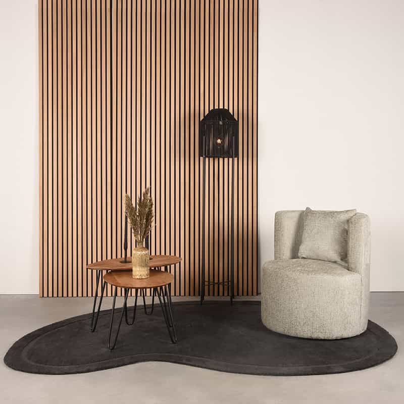 Harig houten wandpaneel met zwart metalen wandlamp, beige fauteuil en salontafel op ronde zwarte vloerkleed in modern interieur.