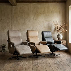 Drie luxe relaxfauteuils in verschillende kleuren, ontworpen voor comfort en stijl, geplaatst in een rustieke woonkamer met houten vloer en natuurlijke decoratie.