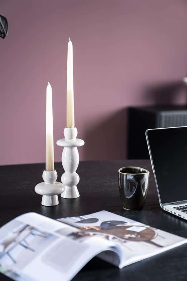 Elegant witte kandelaars op een houten tafel, gecombineerd met een zwarte mok, open magazine en een laptop, passend bij Mokana Meubelen voor een stijlvolle en moderne interieurstijl.