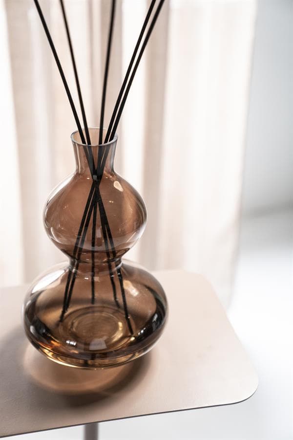 Vaas met zwart riet op een wit tafelblad, modern interieur met zachte verlichting.