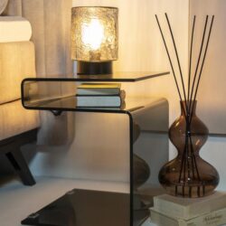 Glazen bijzettafel met zwart frame en warme lamp aan, stijlvolle woonkamer decoratie, modern interieur design, Mokana meubels, elegante kameraccessoires, unieke inrichting, houten en glazen materialen, woonstijl inspiratie.