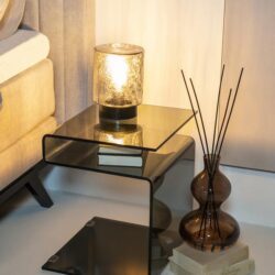 Elegante bijzettafel van glas en zwart met open tussenruimte, ideaal voor modern interieur, gecombineerd met sfeervolle lamp en decoratieve accessoires voor een stijlvolle woonruimte.