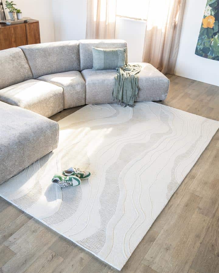 Lichte beige vloerkleed met golvende patronen op houten vloeren in woonkamer met moderne Bank.