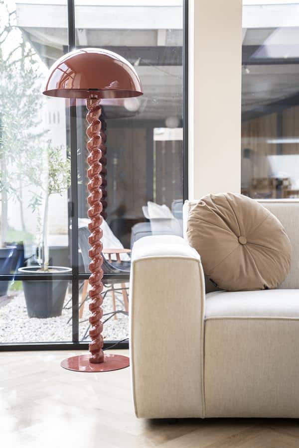 Gedraaide roze vloerlamp naast beige bank in wooninterieur, modern en stijlvol.