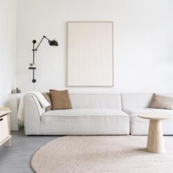 Minimalistisch wit bankstel met zachte beige kussens, moderne zwarte muur lamp en ronde beige tapijt in een strakke, lichte woonkamer van Mokana Meubelen.