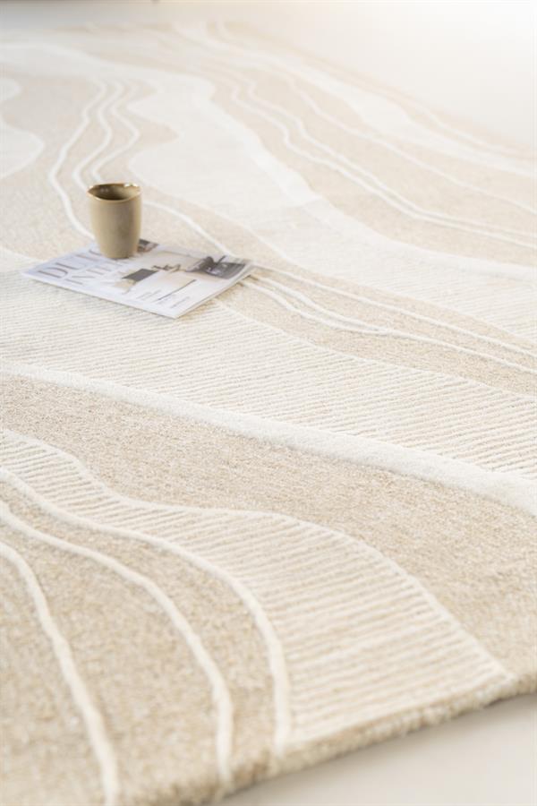 Zachte beige vloerkleed met witte abstracte lijnen, luxe textuur en modern design, perfect voor een stijlvolle woonkamer of slaapkamer.