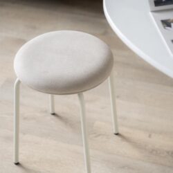 Minimalistisch krukje met beige bekleding en witte metalen poten, ideaal voor moderne interieurinrichting.