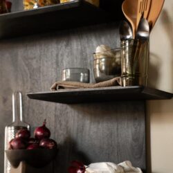 Keukenshelfwand met opbergruimte, keramische bakken met pasta en knoflook, glazen potten, houten keukengerei, rode uien, linnen doek, moderne en functionele keukenopslag, stijlvolle houten wandplanken, keukenorganisatie en decoratie, Mokana Meubelen.