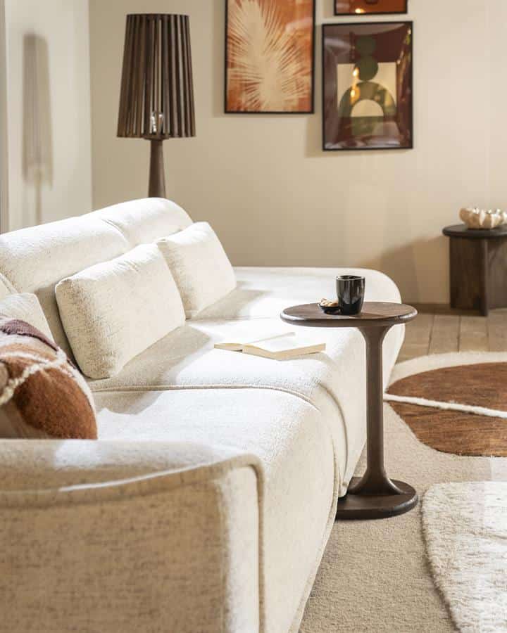 Houten salontafel met zwarte beker en boek op een lichte bank in een gezellige woonkamer.