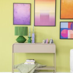 Strakke beige wandtafel met decoratieve groene lamp en vazen, kleurrijke abstracte kunst aan limegroene muur, stijlvolle interieurdecoratie, modern woonstijl, Mokana Meubelen.