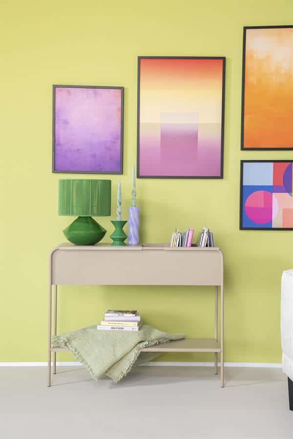 Strakke beige wandtafel met decoratieve groene lamp en vazen, kleurrijke abstracte kunst aan limegroene muur, stijlvolle interieurdecoratie, modern woonstijl, Mokana Meubelen.