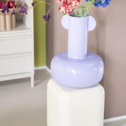 Vaas met kleurrijke bloemen op een modern gestileerde witte en paarse keramische sculptuur in een interieur met pastelkleuren en minimalistisch design.