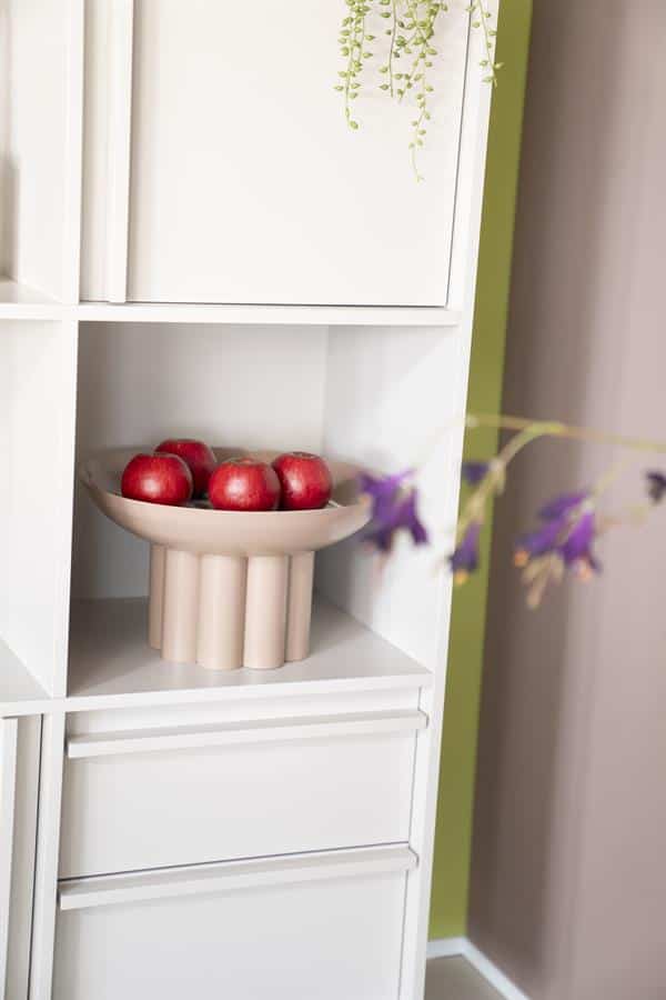Appel centraal op witte boekenkast met keramische fruitschaal en groene muur voor een modern interieur.