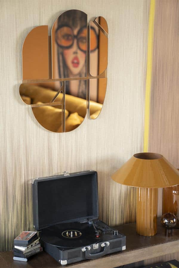 Reflectie van vrouw met grote bril op spiegel, retro interieur met platenspeler en gouden lamp, vintage woonkamer decor, stijlvolle woonaccessoires, nostalgische sfeer, modern design gecombineerd met retro elementen.