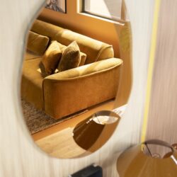 Elegant houten wandspiegel met gouden sofa en accessoires, perfect voor een gezellige woonkamer inrichting. Mokana Meubelen biedt stijlvolle en op maat gemaakte meubeloplossingen.