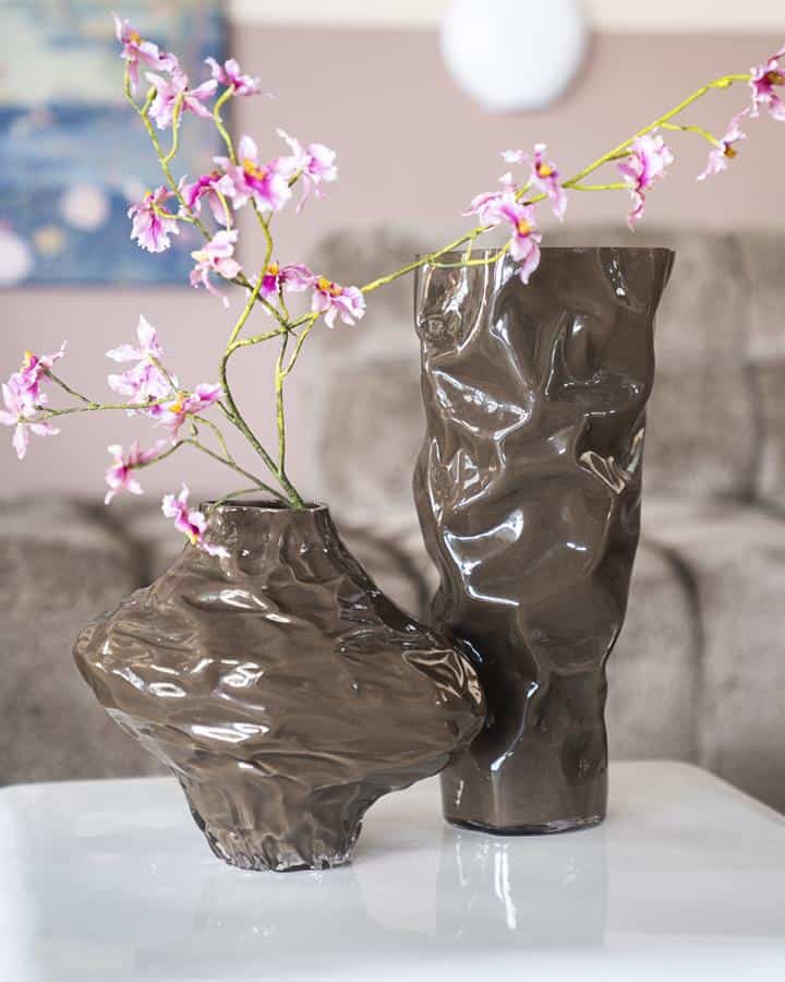 Unieke keramieke vazen met een sculpturale, ruw textuur gevuld met delicate roze bloemen, perfect voor moderne interieurdecoratie.