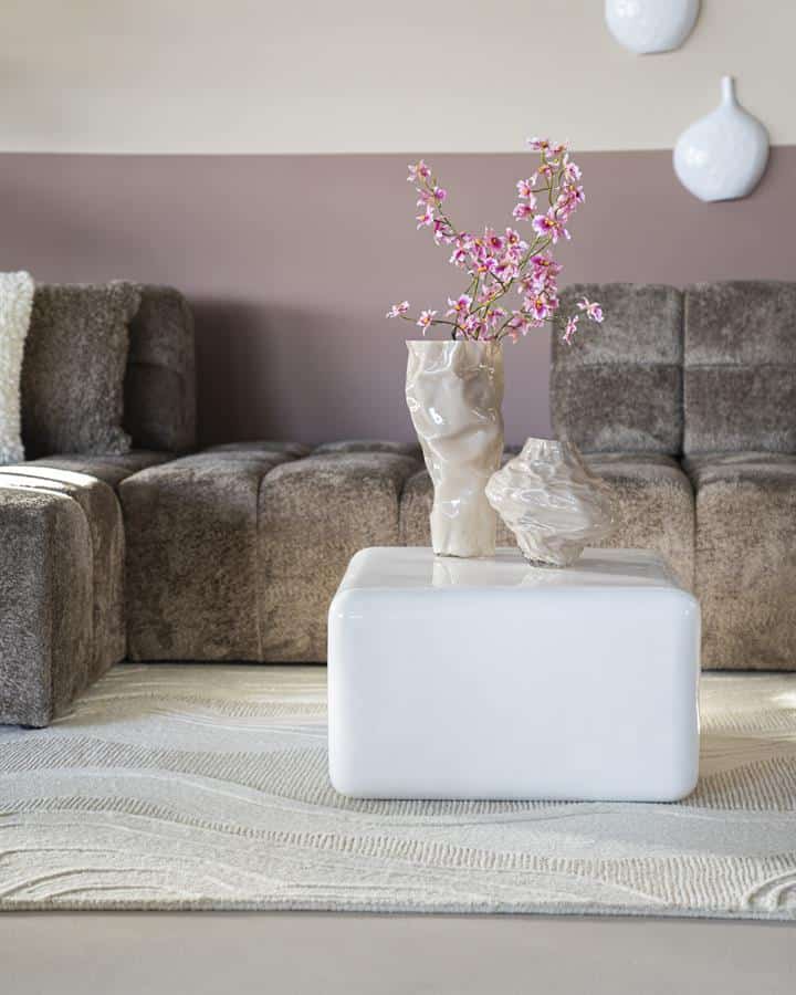 Elegante witte salontafel met keramische vazen en bloemendecor, modern interieur met bank, subtiele kleuren en gezellige sfeer.