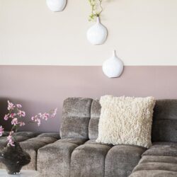 Stijlvolle woonkamer met moderne meubels, zachte kleuren en decoratieve witte vazen met groene takjes. Perfect voor een elegante en gezellige woonruimte.