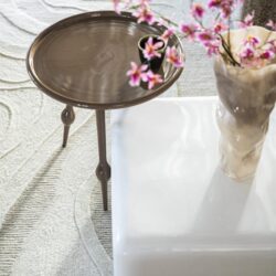 Elegant bijzettafel met rond houtblad en sierlijke poten, gecombineerd met een moderne witte salontafel en een keramieke vaas met pinkbloesems, perfect voor een stijlvolle woonkamer.