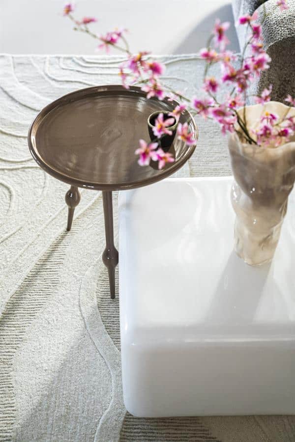 Elegant bijzettafel met rond houtblad en sierlijke poten, gecombineerd met een moderne witte salontafel en een keramieke vaas met pinkbloesems, perfect voor een stijlvolle woonkamer.