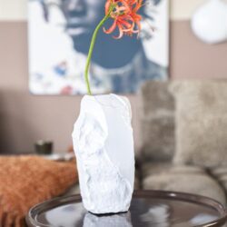 Oranje bloem in witte keramische vaas op ronde houten salontafel, modern interieur met comfortabele bank, decoratief meubelstuk, designvaas, stijlvolle woonaccessoire.