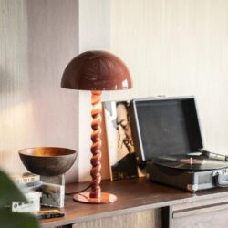 Unieke houten tafellamp met gedraaide standaard op een vintage houten dressoir, naast een platenspeler, decoratieve accessoires en een kunstboek, in een sfeervolle woonkamer.