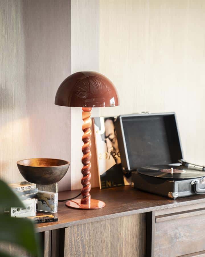 Unieke houten tafellamp met gedraaide standaard op een vintage houten dressoir, naast een platenspeler, decoratieve accessoires en een kunstboek, in een sfeervolle woonkamer.