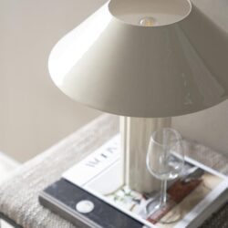 Elegante witte tafellamp met rvs voet op een bijzettafel met woonmagazine en glazen wijnfles, stijlvolle interieurverlichting voor moderne woningen.