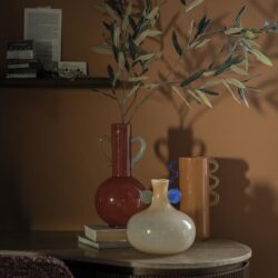 Vazen en decoratieve voorwerpen op een houten tafel met een boekenplank op de achtergrond, stijlvol en modern design van Mokana Meubelen.