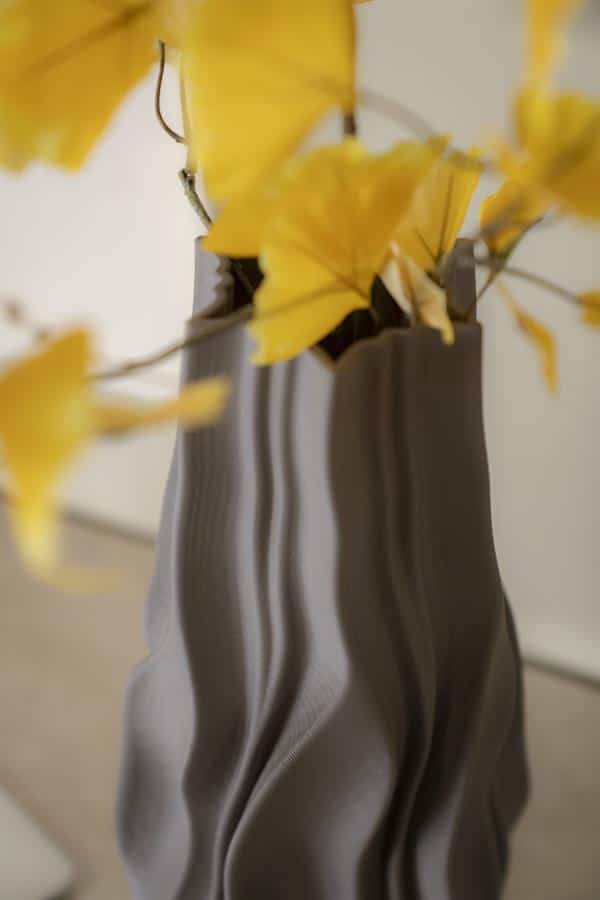 Grote close-up van een elegante, golvende vaas met gele bladeren en bloemen, perfect voor stijlvolle woonkamer decoratie.