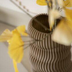 Unieke keramische vaas met ribbelstructuur en gele bloemen, perfect voor stijlvolle interieurdecoratie. Gepositioneerd op een lichte ondergrond voor een frisse look.