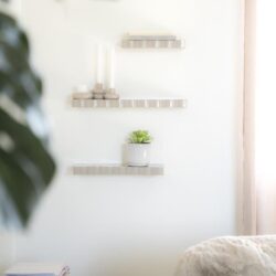 Strakke witte muur met div. decoratieve planken en een plant, stijlvolle en functionele meubels voor een modern interieur.